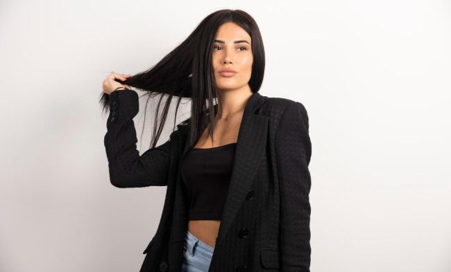 Brunette woman in black crop top playing with her hair.